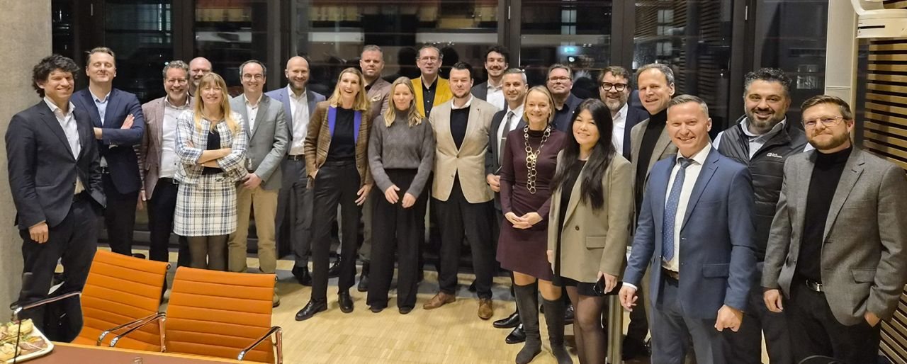 Gruppenfoto von rund zwanzig Teilnehmenden des Roundtables in einem Besprechungsraum mit orangefarbenen Stühlen.